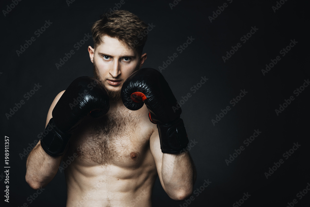 Portrait of young athlete with black gloves on hands looking seriouslyat the camera on a black background. Portrait of young athlete with black gloves on hands looking seriouslyat the camera on a black background.