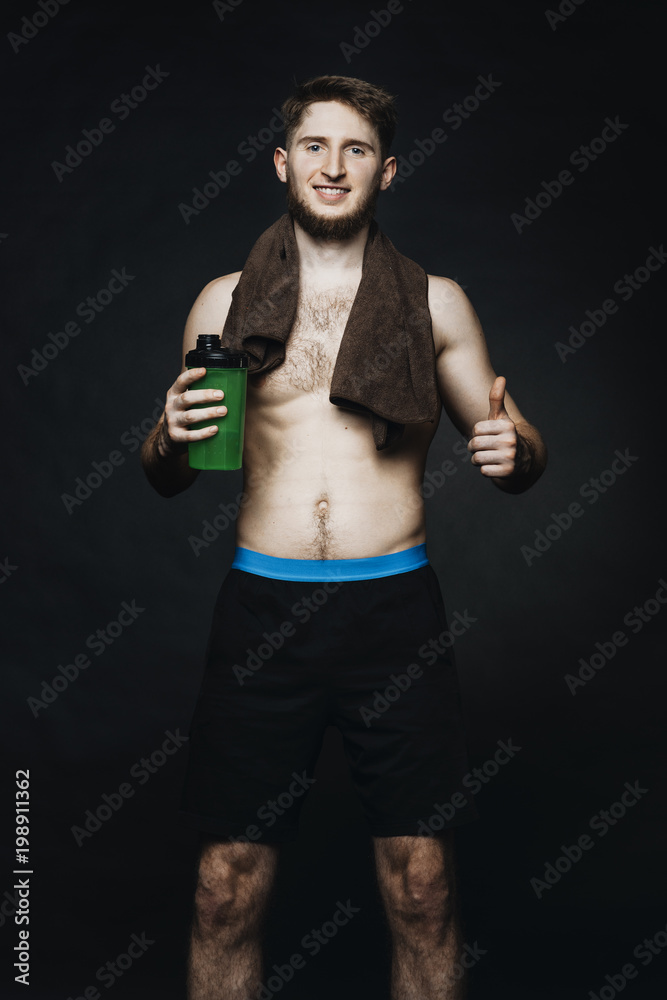 Attractive young man with water bottle in hand and towel around the neck smilling at the camera.Sportsman in a studio on a black background.