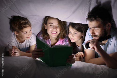 Принти на полотні Happy family reading bedtime story under blanket in evening