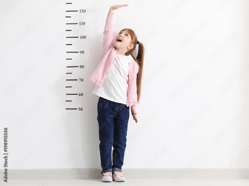 Little girl measuring height near white wall - obrazy, fototapety, plakaty 
