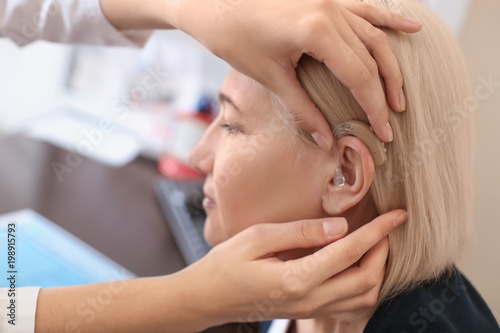 Otolaryngologist putting hearing aid in woman's ear in hospital photo
