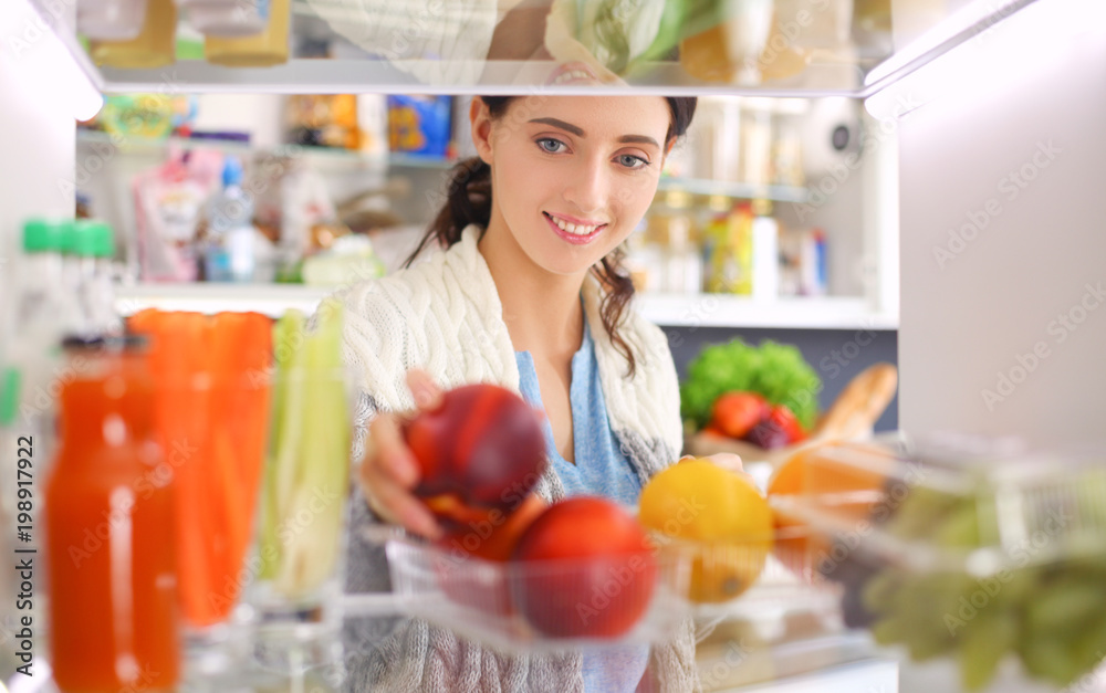 Portrait of female standing near open fridge full of healthy food, vegetables and fruits. Portrait of female Portrait of female standing near open fridge full of healthy food, vegetables and fruits. Portrait of female