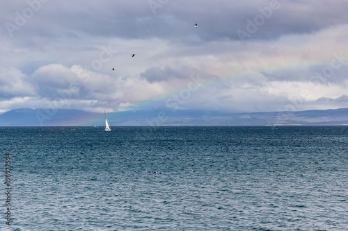 Sail boat at sea, seen from distance in stormy skies. Rainbow on the side