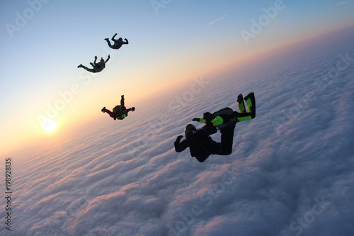 Skydivers are flying above pink clouds.