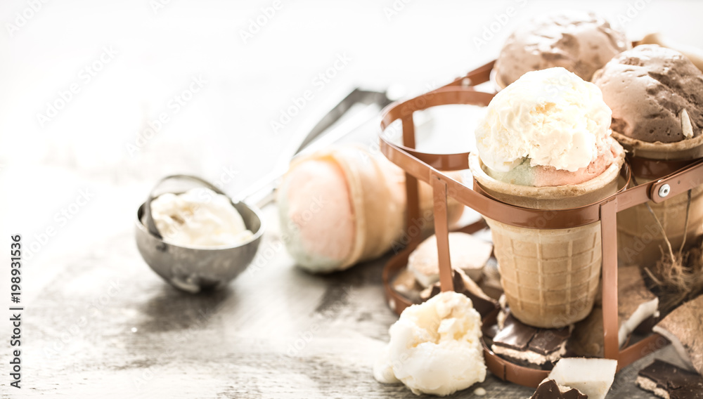 Fototapeta premium different ice cream in a cone stands in a beautiful stand on a wooden light background, a concept of summer sweets and ice cream