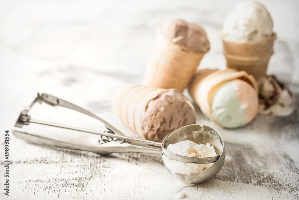 different ice cream in a cone stands on a wooden light background, the concept of summer sweets and ice cream different ice cream in a cone stands on a wooden light background, the concept of summer sweets and ice cream