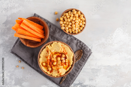 Hummus, fresh carrot sticks and boiled chickpeas in wooden bowls. Vegan food concept, light background, copy space, top view