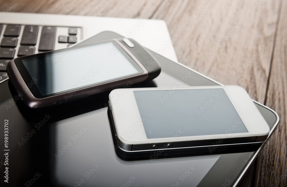 keyboard with two phones and tablet pc on wooden desk