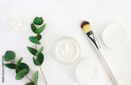 Skincare cosmetics with aroma eucalyptus plant extract. Jar of organic beauty product and application brush with fresh green leaves herbal bough, top view white background. Home spa and body care