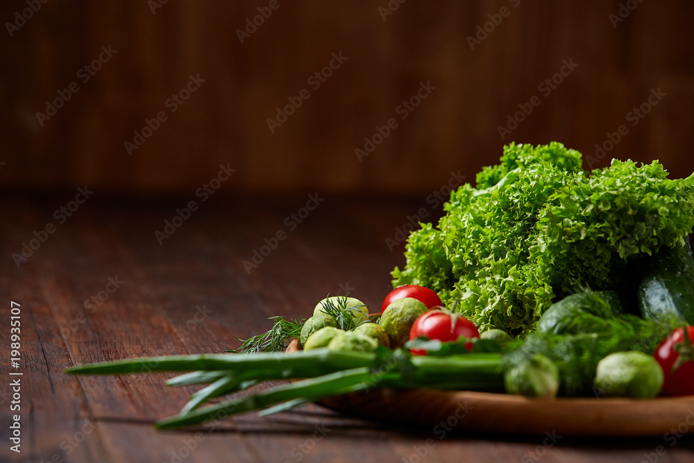 Vegetarian still life of fresh vegetables on wooden plate over rustic background, close-up, flat lay.