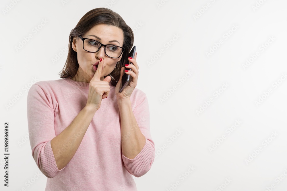 Portrait of a woman tells secrets and gossip on the cell phone. Background white, studio, copy space Portrait of a woman tells secrets and gossip on the cell phone. Background white, studio, copy space