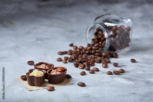 Side view of overturned glass jar with coffee beans and chocolate candies on white background, selective focus photo