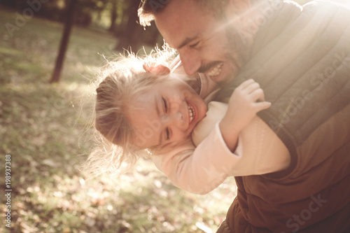 Smiling happy father playing with daughter in park and hugging her.