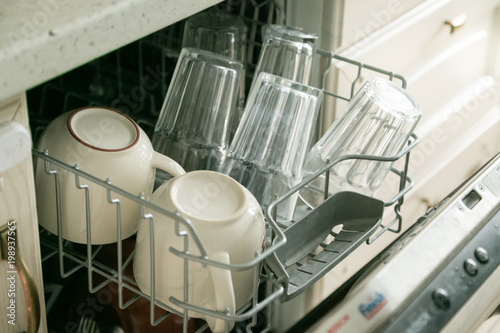 Dishwasher full with clean dishes in kitchen background