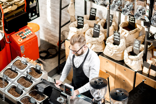 Fotografija Sales man standing at the counter in the coffee store with roaster machine on th