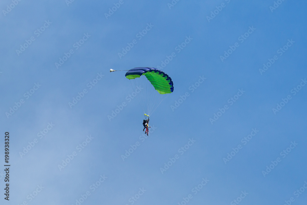 Parachutists: Instructor and Beginner with Green Parachute against Clear Blue Sky Parachutists: Instructor and Beginner with Green Parachute against Clear Blue Sky