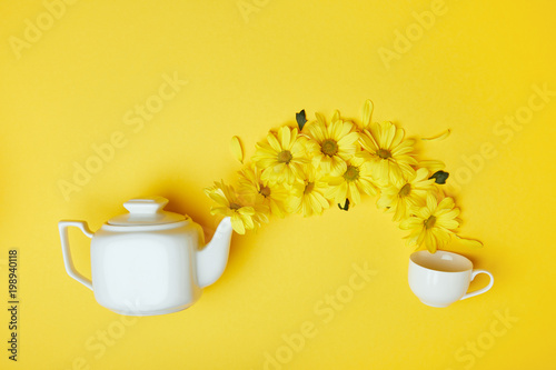 Yellow chrysanthemums pouring into cup from white pot isolated on yellow