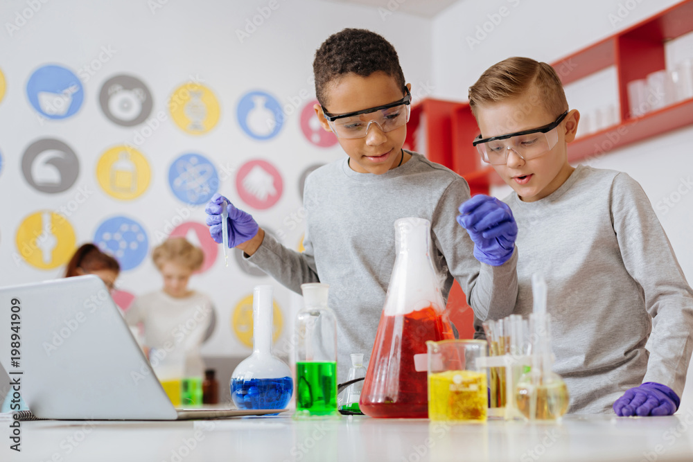Love experimenting. Two pleasant teenage friends adding chemicals into the flask with a pipette and observing the reaction during their chemistry class in the lab Love experimenting. Two pleasant teenage friends adding chemicals into the flask with a pipette and observing the reaction during their chemistry class in the lab