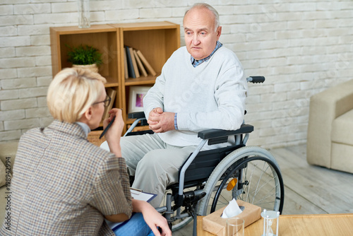 High angle portrait of disabled senior man in wheelchair sharing problems with psychiatrist during therapy session, copy space