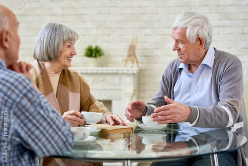 Group of senior people chatting and drinking tea enjoying time in retirement home  copy space