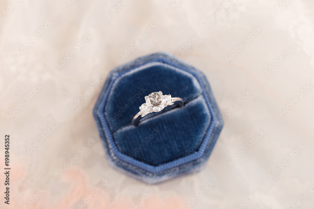 White golden wedding ring with diamonds in blue vintage velvet ring box on pink lace background