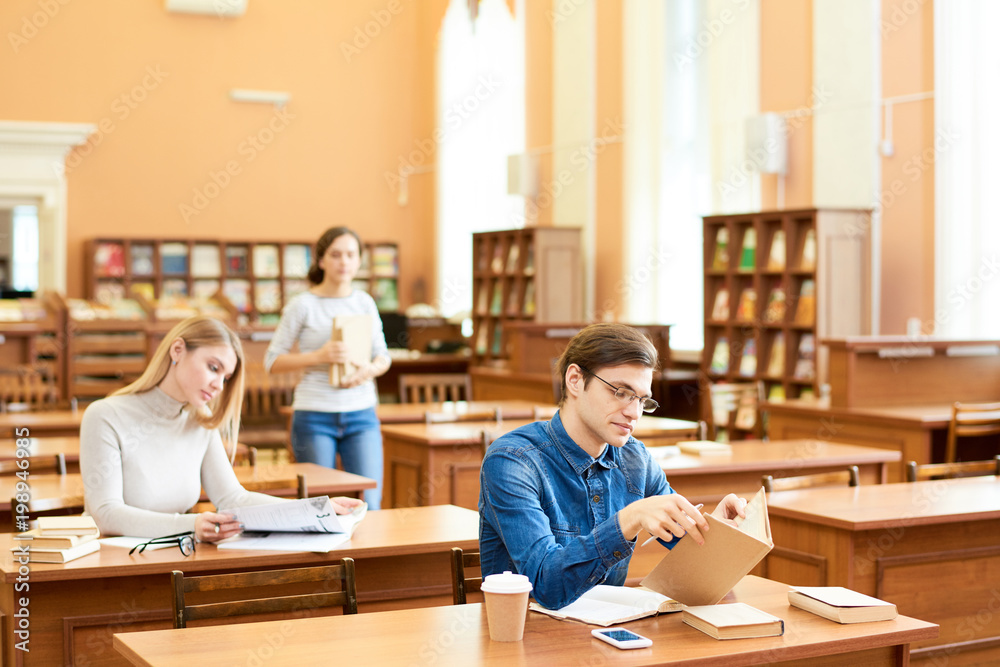Busy concentrated students sitting at wooden tables and studying scientific publications and summarizing information in modern library Busy concentrated students sitting at wooden tables and studying scientific publications and summarizing information in modern library