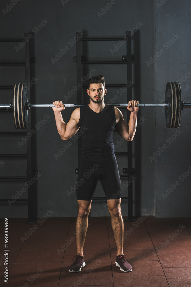 Front view of young sportsman holding barbell on shoulders in gym Front view of young sportsman holding barbell on shoulders in gym