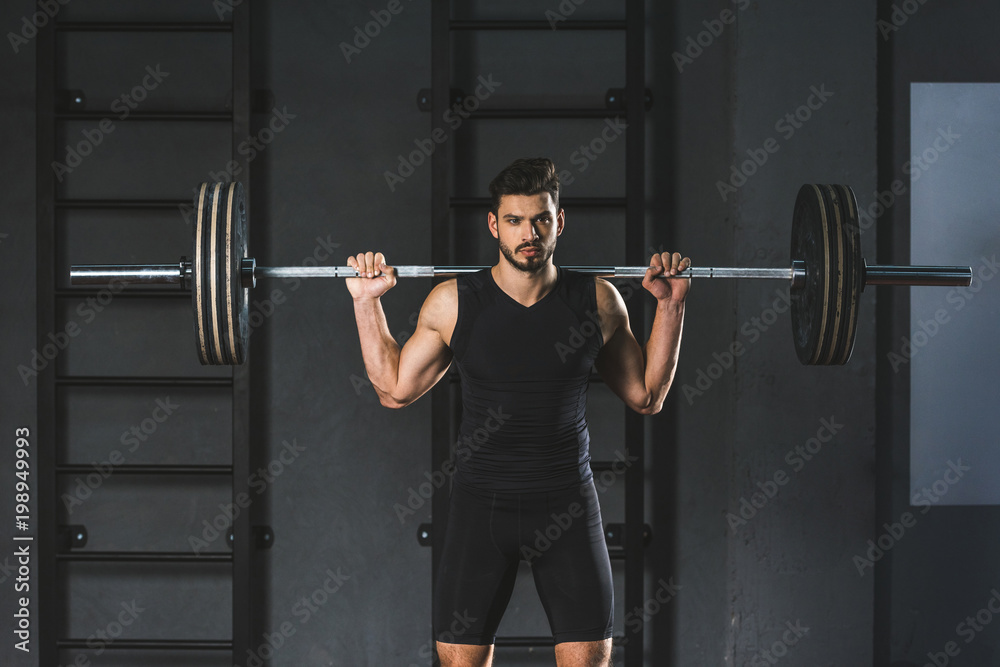 Young sportsman holding barbell on shoulders in gym Young sportsman holding barbell on shoulders in gym
