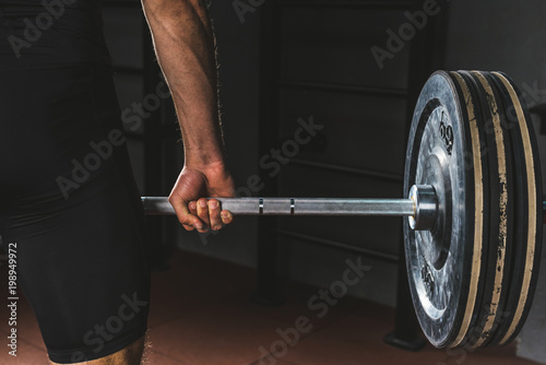 Cropped image of sportsman holding barbell in gym