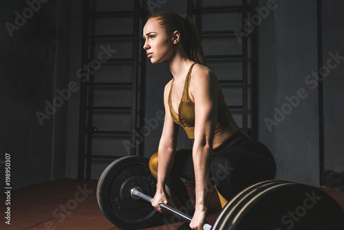 Side view of young bodybuilder preparing to raise barbell in gym