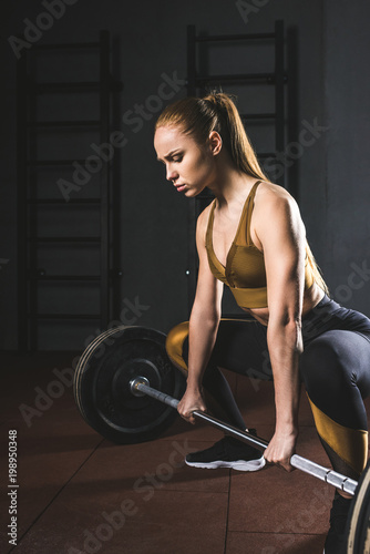 Young female bodybuilder preparing to raise barbell in gym