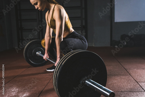 Cropped image of young sportswoman prepare to raise barbell in gym