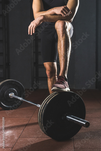 Cropped image of resting sportsman standing on barbell in gym photo