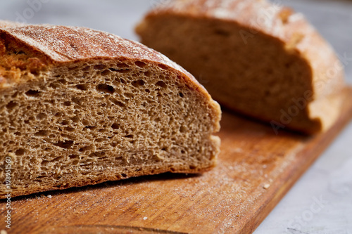 Fresh rye bread loaf on a wooden chopping board over white textured background, shallow depth of field