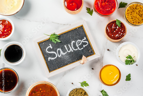 Set of different sauces - ketchup, mayonnaise, barbecue, soy, teriyaki, mustard, grain hills, pesto, adzhika, chutney, tkemali, pomegranate sauce on white marble background. Top view copy space