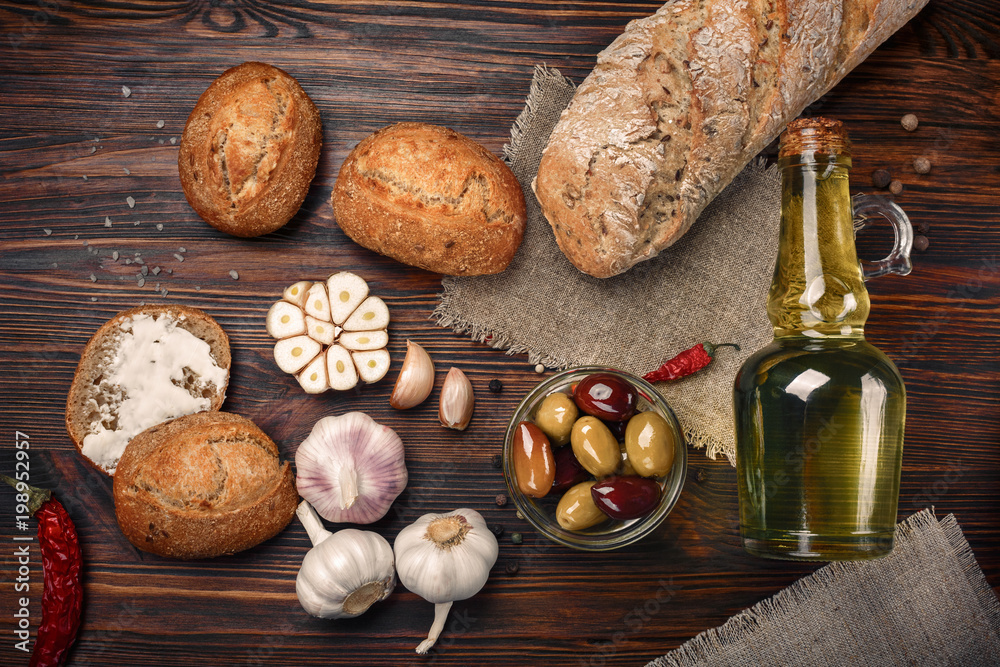 Fototapeta premium Olives in oil with spices in glass vase and bread on table