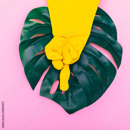 a hand in a yellow glove depicts an aggressive gesture of fuck you on pink background with palm. minimalism and surrealism