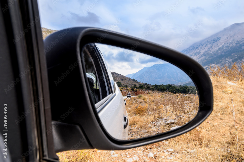 View of the mountain landscape from the car window on the road in Greece, Crete. Reflection in the mirror. Tourist trip by car.