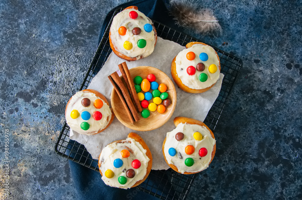 Classic cinnamon rolls - cinnabons with cream cheese frosting with smarties. Blue stone background. Top view. Classic cinnamon rolls - cinnabons with cream cheese frosting with smarties. Blue stone background. Top view.
