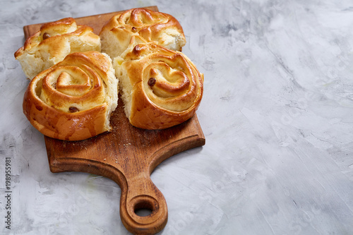 Homemade rose buns on wooden cutting board over white textured background, close-up, shallow depth of field photo