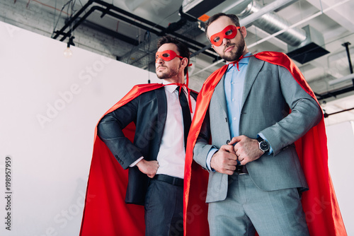 low angle view of handsome super businessmen in red masks and capes in office