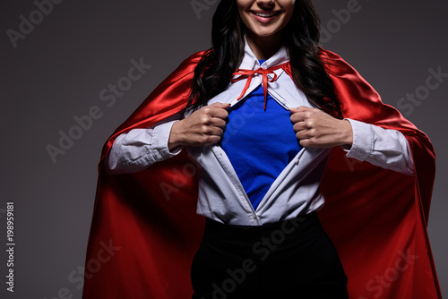 Φωτογραφία cropped image of super businesswoman in red cape showing blue shirt isolated on
