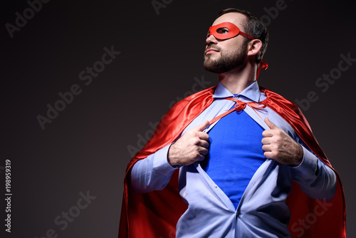 handsome super businessman in mask and cape showing blue shirt and looking away isolated on black