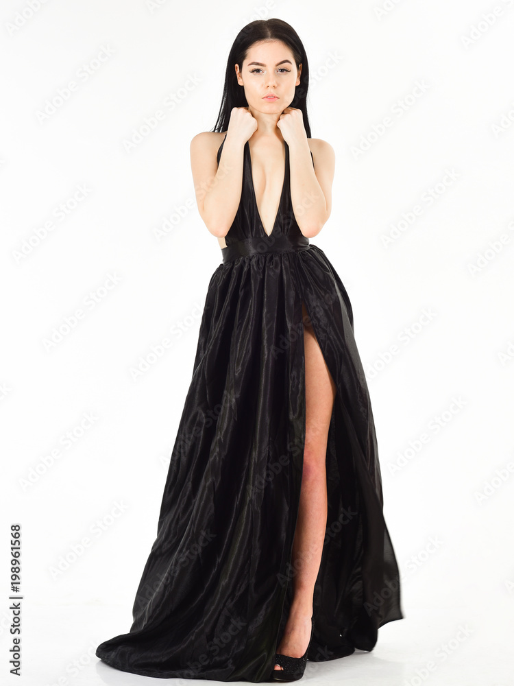 Lady, sexy girl in dress. Woman in elegant black long evening dress with decollete, white background. Attractive girl wears expensive fashionable evening dress with erotic slit. Fashion dress concept.