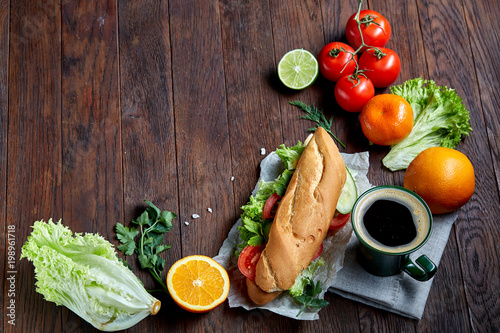 Fresh sandwich with lettuce, tomatoes, cheese on wooden plate, cup of coffee on wooden background, selective focus photo