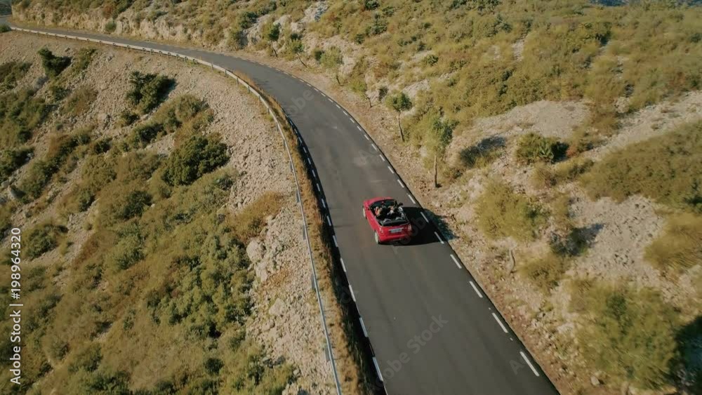 Amazing epic inspiring travel drone aerial shot following red convertible car with friends on empty mountain scenic road driving into sunset, concept tourism destination and summer adventures