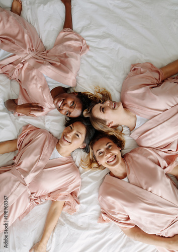 Bride with bridesmaids lying on bed and smiling