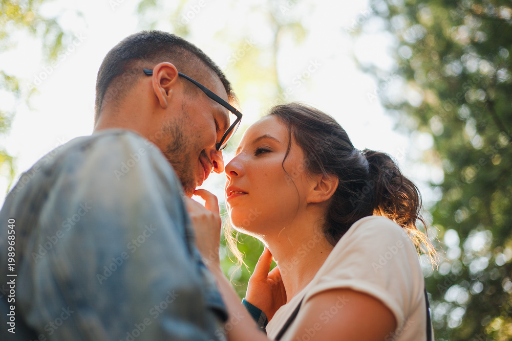 Beautiful young couple kiss and hug in a summer park near trees