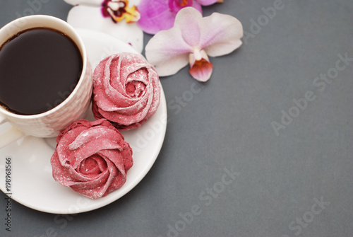 Sweet Pink Meringues and Cup of Coffee on Blue Gray background with Orchid Flowers. Spring Background with copy space. Breakfast.