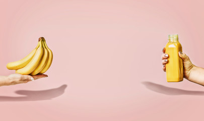 Summer food and beverages background with bananas and yellow drink bottle in female hand at pastel pink background, front view, banner or template.